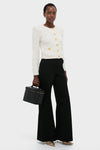 Model with a classic, high-end CHANEL Large Caviar Vanity Bag, wearing an effortless cream-white cardigan, black wide-leg trousers, and fun metallic gold-striped shoes.
