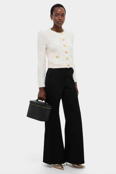 Model with a classic, high-end CHANEL Large Caviar Vanity Bag, wearing an effortless cream-white cardigan, black wide-leg trousers, and fun metallic gold-striped shoes.