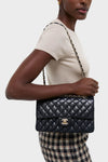 Person wearing a light top and checked bottoms, effortlessly carrying a classic CHANEL Navy Blue Lambskin Double Flap bag, showcasing high-end style with a fun, chain-woven strap.