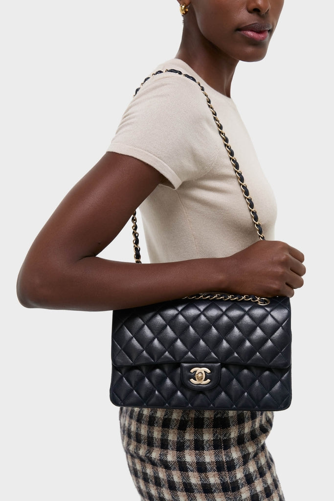 Person wearing a light top and checked bottoms, effortlessly carrying a classic CHANEL Navy Blue Lambskin Double Flap bag, showcasing high-end style with a fun, chain-woven strap.