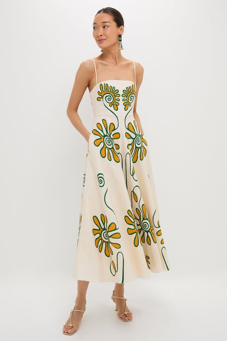 Woman models the Namur Ivory Delta Dress, a classic midi-length piece with an effortless daisy print, styled with tassel earrings and sandals for a fun, high-end look.
