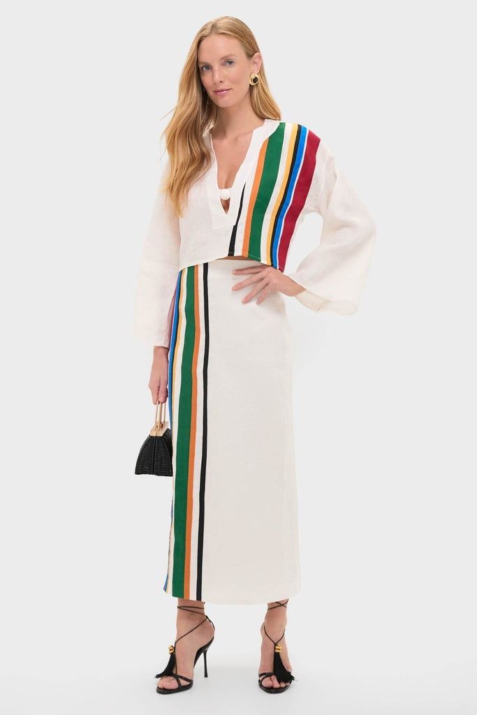 Model in Roman Sassari Top, a classic, effortless ensemble with vibrant stripes, paired with a matching skirt, black handbag, gold hoops, and strappy sandals. High-end, resort-inspired style.