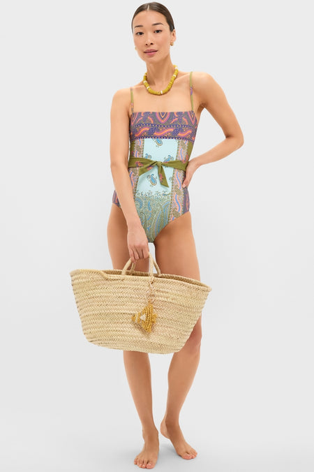 Pastel Patchwork Lucent One Piece on model with paisley prints, classic straw tote, and chunky necklace. Features full coverage, adjustable straps, embodying effortless, fun, high-end style.