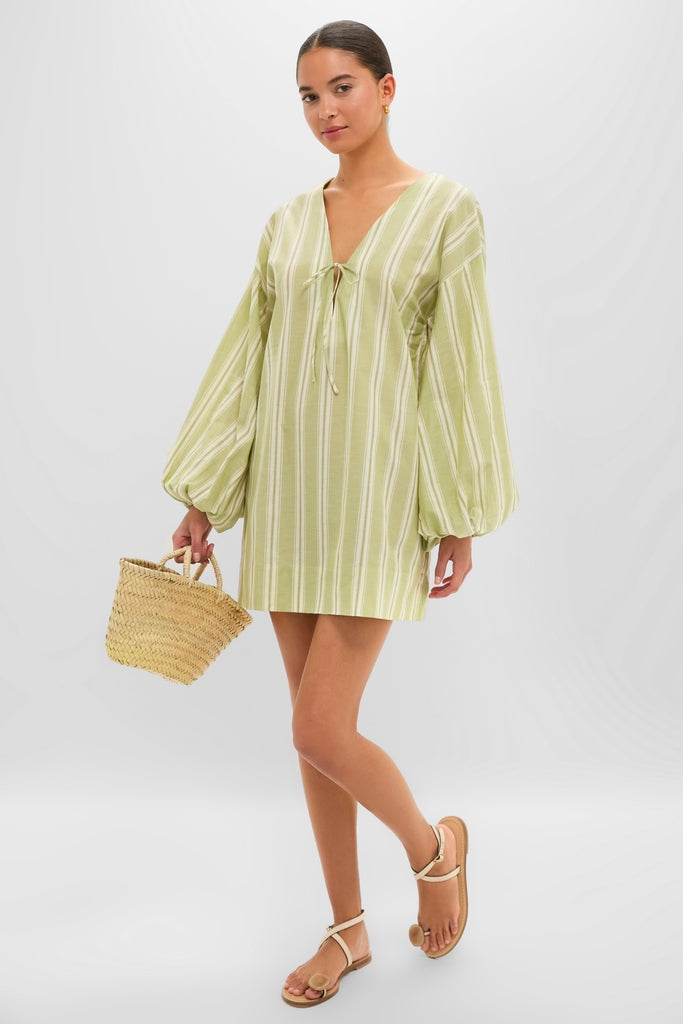 Young woman models the Faded Juniper Ombre Stripe Pia Mini Dress, featuring classic puff sleeves and a relaxed fit, styled effortlessly with sandals and a straw tote.