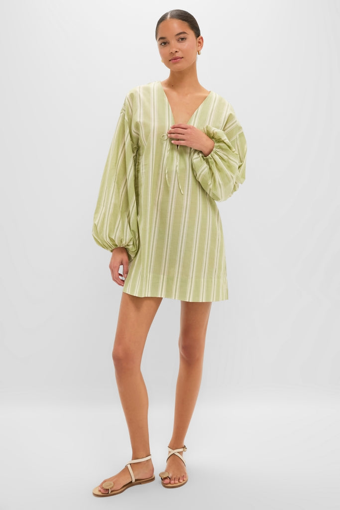 Woman in a Faded Juniper Ombre Stripe Pia Mini Dress with puff sleeves and tie neckline, styled with effortless tan sandals, embodying a classic, high-end, fun resort look.