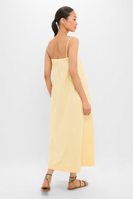 Woman models the classic Banana Lopez Midi Dress in buttery yellow, showcasing an effortless A-line silhouette with adjustable straps and box-pleat detail, paired with fun, high-end sandals.