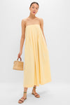 Model wearing classic Banana Lopez Midi Dress with adjustable straps and box pleats, styled effortlessly with a straw handbag and multicolored sandals for a high-end, fun look.
