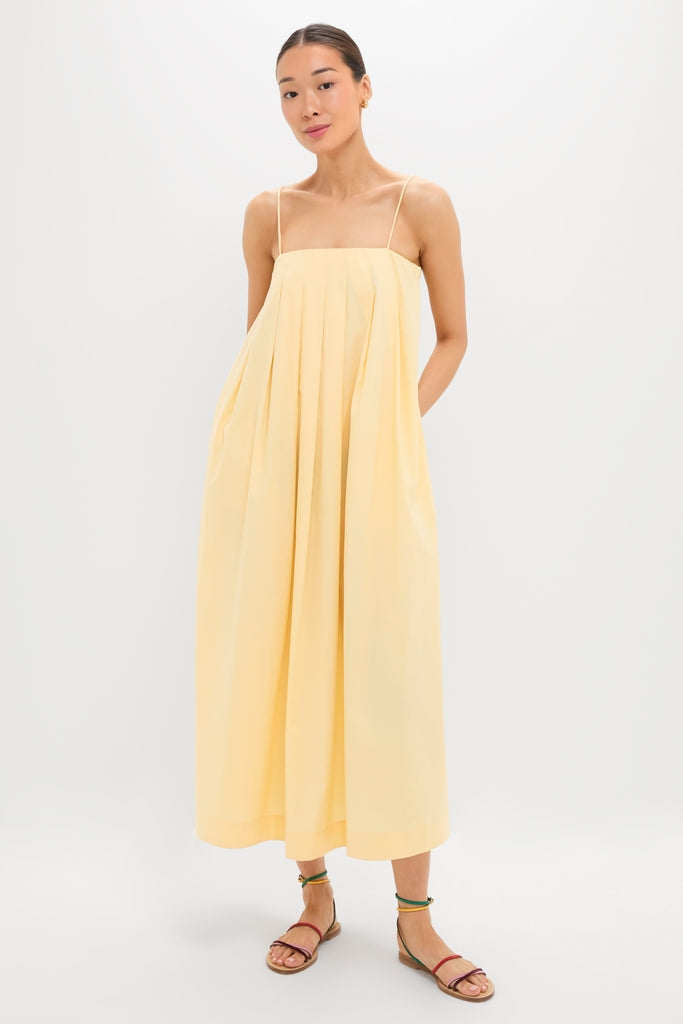 Person models the classic Banana Lopez Midi Dress, showcasing an effortless A-line silhouette with adjustable straps and box pleats, styled with gold hoops and colorful sandals.
