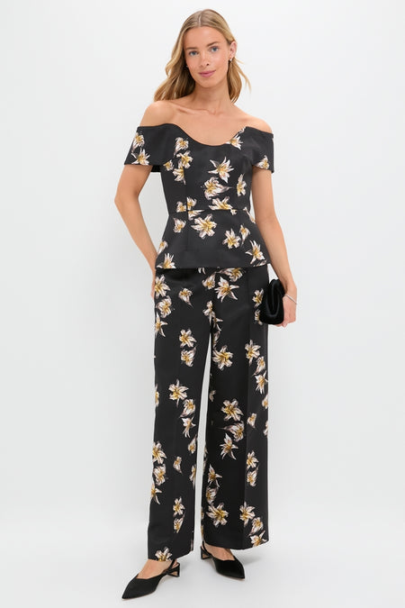 Model in the Black and Yellow Souline Top, an off-shoulder peplum blouse with matching high-waisted, wide-leg pants, carrying a black clutch and wearing slingback heels.