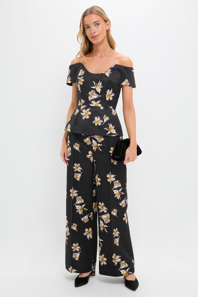 Woman models Black and Yellow Daffy Trousers, an effortless, high-end two-piece with a lily print. She's accessorized with a clutch, heels, and minimal jewelry.