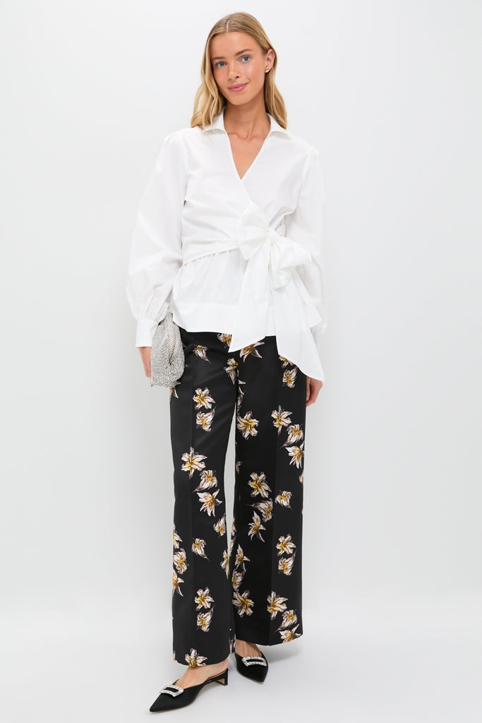 Model wearing classic Black and Yellow Daffy Trousers with scattered lilies, paired effortlessly with a white wrap blouse, mule heels, and a high-end silvery clutch.