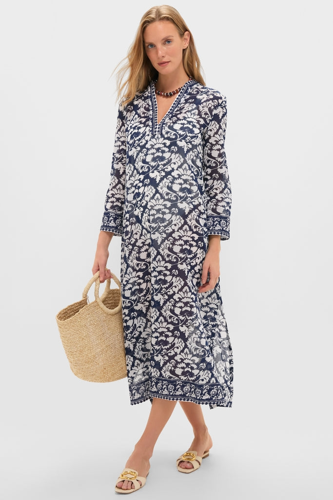 Woman in a classic Dark Blue Giada Caftan, featuring a floral pattern and split V-neck, accessorized with a straw tote bag and sandals, exuding effortless, high-end style.