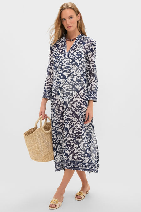Woman in a classic Dark Blue Giada Caftan, featuring a floral pattern and split V-neck, accessorized with a straw tote bag and sandals, exuding effortless, high-end style.