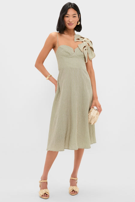 Woman models the Green Striped Monsterea Leaf Sleeveless Midi Dress with a sweetheart neckline, bow detail, and spaghetti strap, paired with a woven clutch and braided sandals.