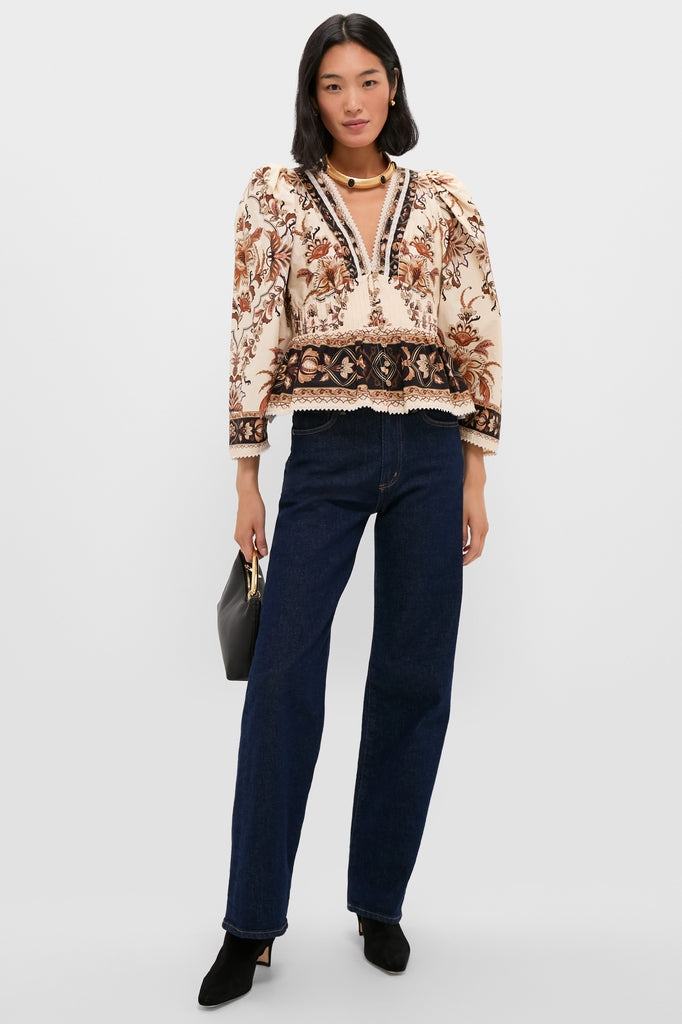 Woman wearing the Majestic Garden Sand Blouse, a classic bohemian-style top with floral embroidery, paired with high-waisted jeans and accessories, creating an effortless, high-end look.