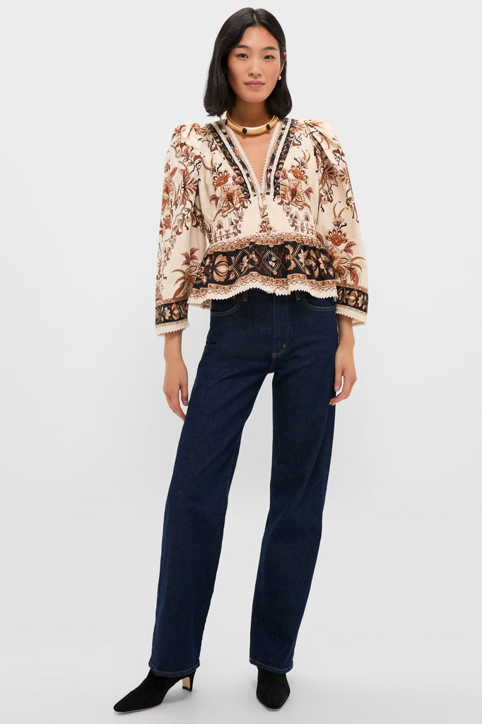 Woman in Majestic Garden Sand Blouse with floral-paisley print, pairing classic style with effortless, high-end flair, complemented by dark-wash jeans and black ankle boots.