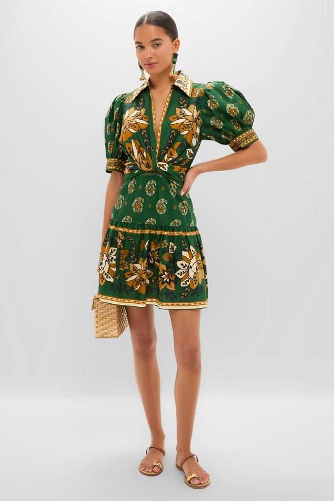 Young woman in Ayla Green Mini Dress with floral motifs, puffed sleeves, and tiered skirt, carrying a woven straw handbag, embodying classic, effortless style.