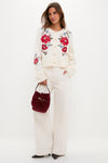 Model wears the classic Cream Flowers Embroidered Knit Cardigan, featuring intricate floral detailing, paired with high-waisted trousers and a burgundy handbag for an effortless, high-end look.