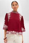 Woman models the Burgundy Bicolor Palm Tree Embroidery Blouse, featuring white floral embroidery and scalloped edges, paired with cream trousers for an effortlessly classic and high-end look.