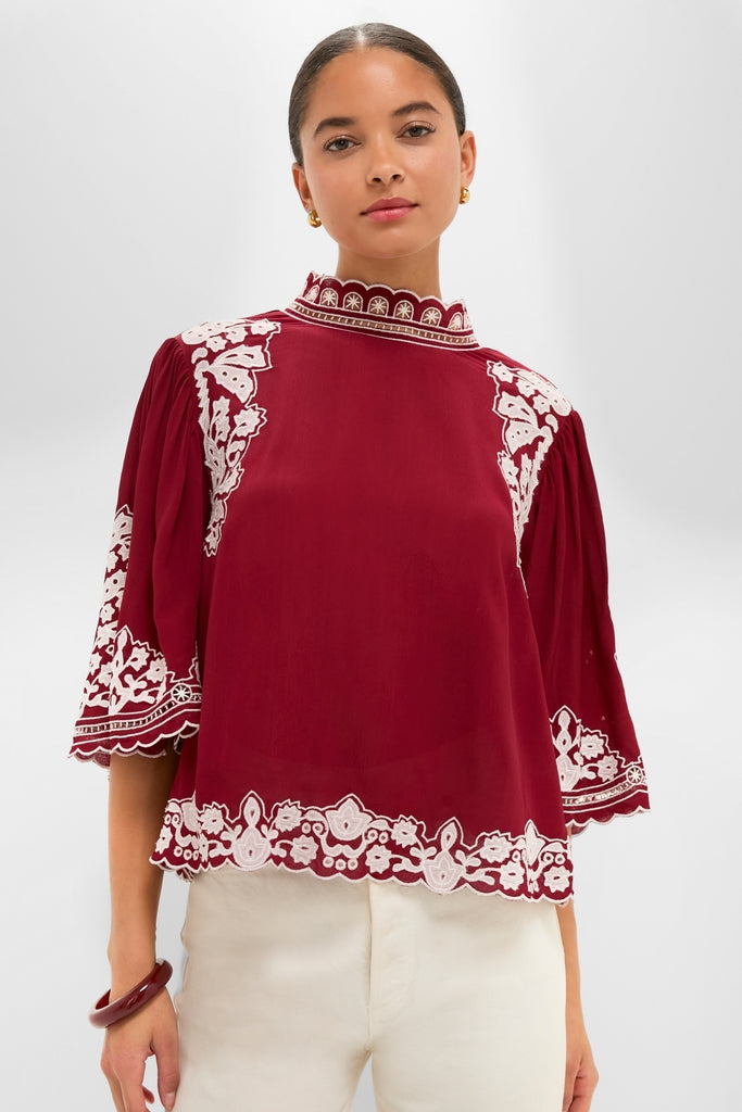 Woman models the Burgundy Bicolor Palm Tree Embroidery Blouse, featuring white floral embroidery and scalloped edges, paired with cream trousers for an effortlessly classic and high-end look.