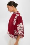 Woman in profile wearing the Burgundy Bicolor Palm Tree Embroidery Blouse, featuring a high-neck, loose fit, scalloped edges, and white floral details, paired with light pants for an effortless, classic look.