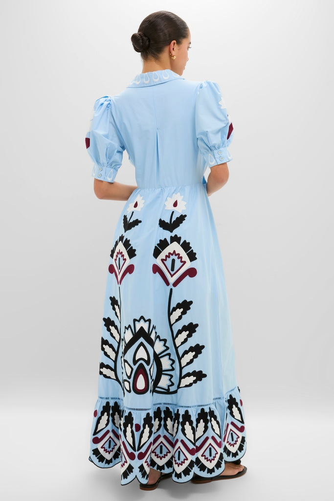 Woman in a Blue Artisanal Short Sleeve Maxi Dress, featuring classic puffed sleeves and an effortlessly full skirt with fun, high-end floral and geometric motifs.