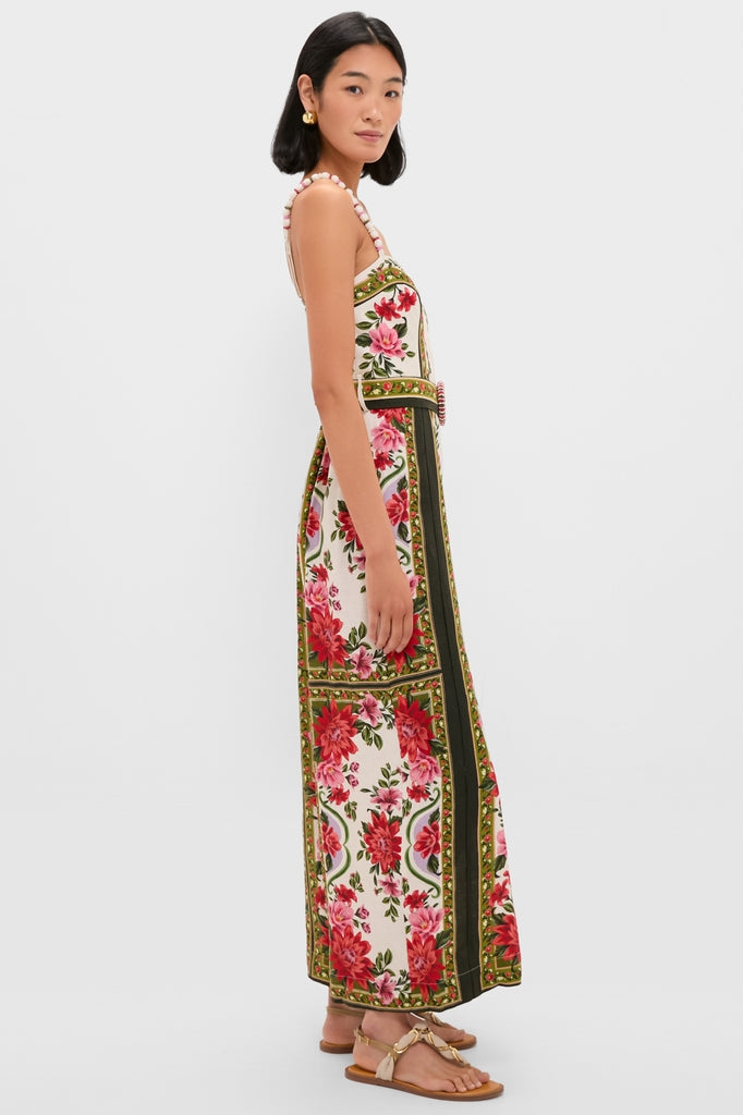 Wonder Rio Sand Sleeveless Maxi Jumpsuit, featuring a bold floral print with pom-pom shoulder straps and a belted waist, styled effortlessly with gold-accented sandals.