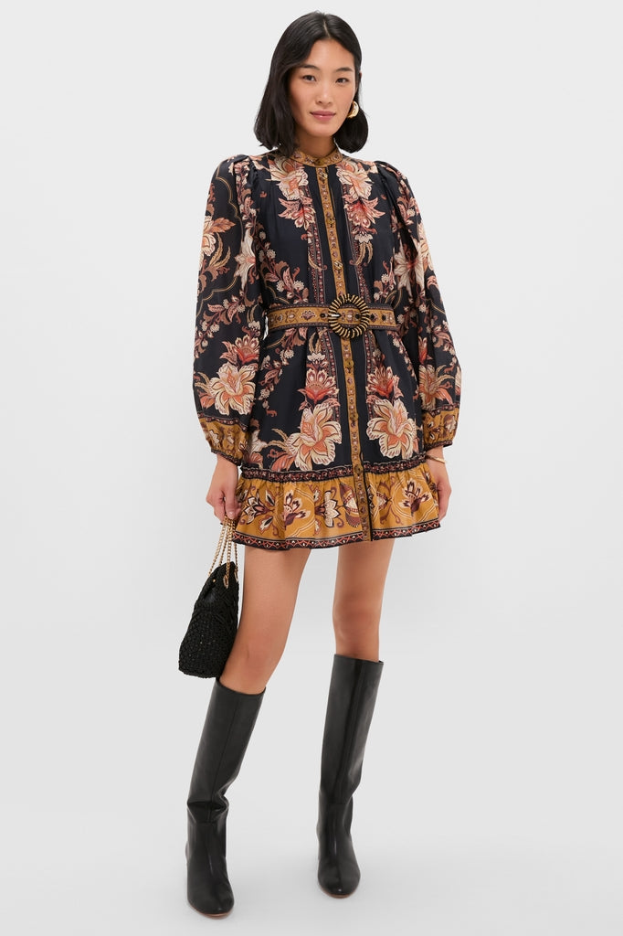 Woman models the Majestic Garden Black Mini Dress, featuring an effortless floral print, cinched waist, and paired with high-end black knee-high boots and a textured handbag.