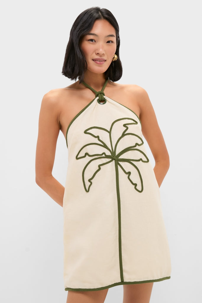 Person wearing the classic Sand Coconut Sleeveless Mini Dress featuring an effortless halter-neck style and fun dark green palm-tree design, embodying high-end simplicity and charm.