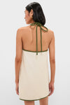 Woman in a Sand Coconut Sleeveless Mini Dress with olive-green binding, showcasing a halter knot design. Classic, effortless style aligned with Tuckernuck's high-end, fun fashion ethos.