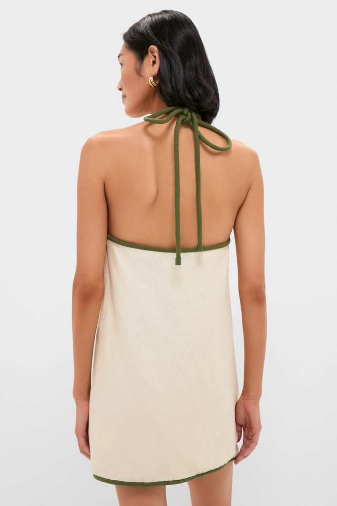 Woman in a Sand Coconut Sleeveless Mini Dress with olive-green binding, showcasing a halter knot design. Classic, effortless style aligned with Tuckernuck's high-end, fun fashion ethos.