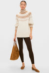 Woman models the classic Ivory Camel Estelle Fair Isle Turtleneck, showcasing its effortless, high-end design with ribbed finishes, paired with chic brown leggings and suede accessories.