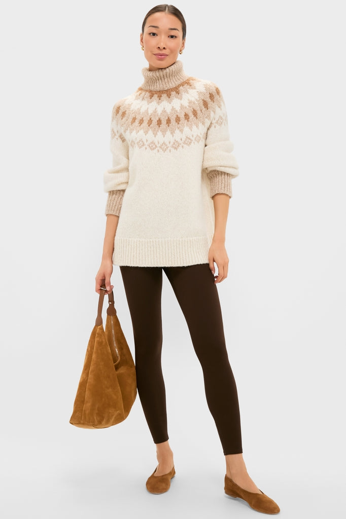 Woman models the classic Ivory Camel Estelle Fair Isle Turtleneck, showcasing its effortless, high-end design with ribbed finishes, paired with chic brown leggings and suede accessories.