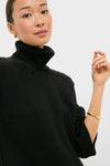 Person wearing Black Louisa Turtleneck Sweater with a classic foldover neck and intricate cable-knit detailing, paired with a gold hoop earring and bangle for an effortless, high-end look.