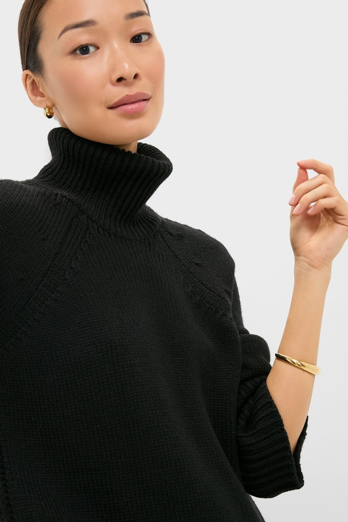 Person wearing Black Louisa Turtleneck Sweater with a classic foldover neck and intricate cable-knit detailing, paired with a gold hoop earring and bangle for an effortless, high-end look.