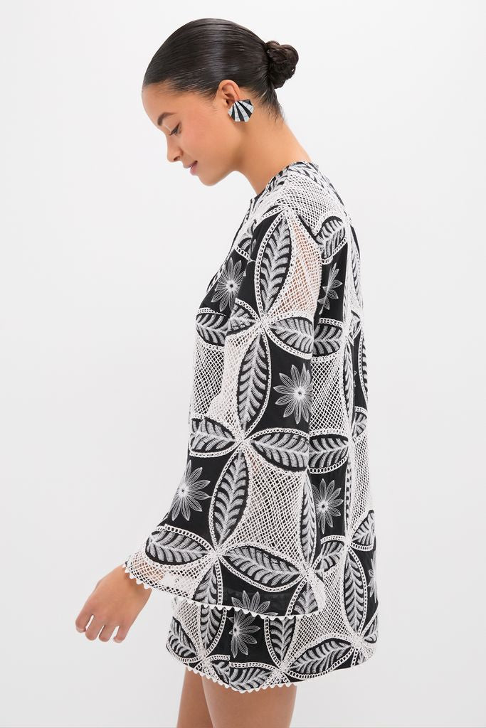 Young woman in profile wearing the Black Plain Gia Mini Dress, showcasing a classic, effortless black-and-white geometric lace pattern, paired with matching high-end earrings for a fun look.