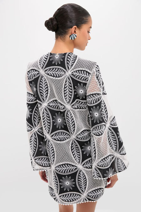 Woman in a Black Plain Gia Mini Dress with geometric floral embroidery, exuding an effortless, high-end style, complemented by oversized earrings.