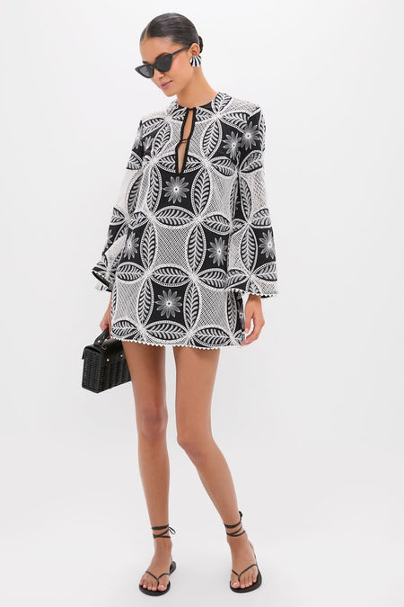 Model wearing the classic Black Plain Gia Mini Dress with geometric/floral lace pattern, long sleeves, keyhole neckline; styled with a structured handbag and thong sandals for an effortless, high-end look.