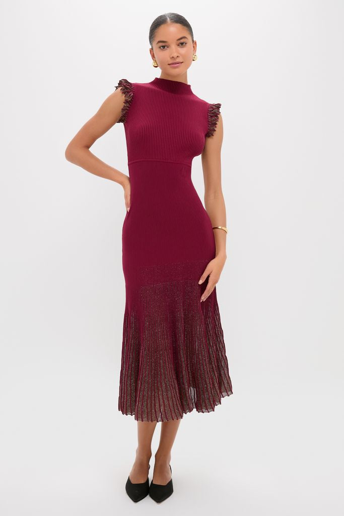 Model wearing the Plum Shimmer Knit Midi Dress, a classic, effortless midi with a mock neckline and pleated skirt, styled with black shoes and minimal gold jewelry for a high-end look.