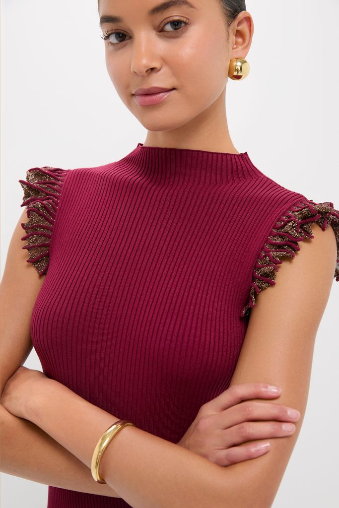 Woman models the Plum Shimmer Knit Midi Dress with a classic mock neckline, ruffled cap sleeves, and subtle metallic fringe, accessorized with chunky gold jewelry for an effortless, high-end look.