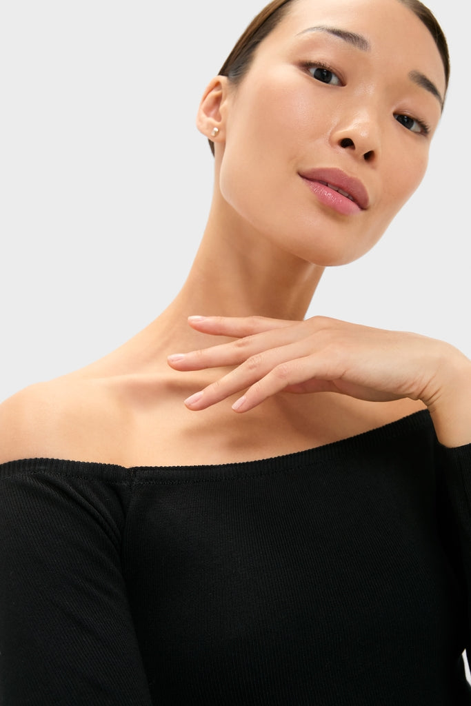 Young woman in a classic, effortless black off-the-shoulder top, embodying high-end style and fun elegance, reflecting Tuckernuck's cool, confident aesthetic.