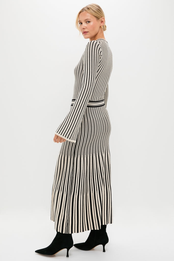 Model in profile wearing the Black and Ivory Striped Maxi Dress, a classic, fitted knit dress with pleated skirt, paired with black suede ankle boots for an effortless, high-end look.