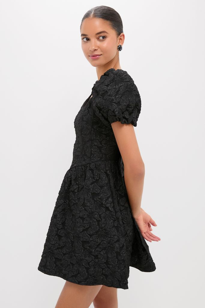 Young woman in profile wearing the Black Jacquard Mini Dress with puffed sleeves and flared skirt, embodying classic, effortless style and a high-end, fun look.