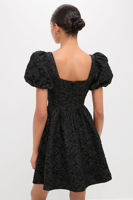 Woman in a classic Black Jacquard Mini Dress with an effortless flared skirt and puffed sleeves, embodying high-end fashion and fun style.