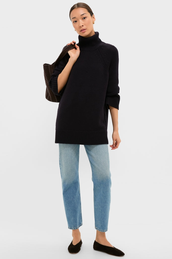Woman wearing classic Navy Louisa Turtleneck Sweater with side cable-knit detail, paired with light jeans, embodying effortless, high-end style; an essential for fun, confident dressing.