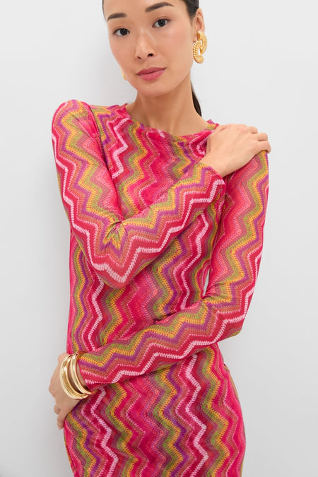 Woman in the Electric Wave Pink Scarlet Maxi Dress, featuring a bold zigzag pattern, accessorized with chunky gold hoop earrings and bangles for a classic, effortless, high-end look.