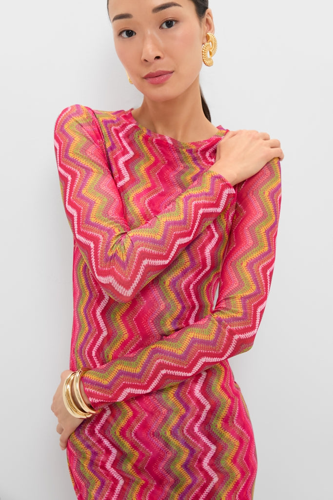 Woman in the Electric Wave Pink Scarlet Maxi Dress, featuring a bold zigzag pattern, accessorized with chunky gold hoop earrings and bangles for a classic, effortless, high-end look.