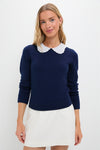 Young woman wearing the classic Navy Violette Sweater with eyelet collar and keyhole closure, styled effortlessly with a white skirt, embodying fun and high-end sophistication.