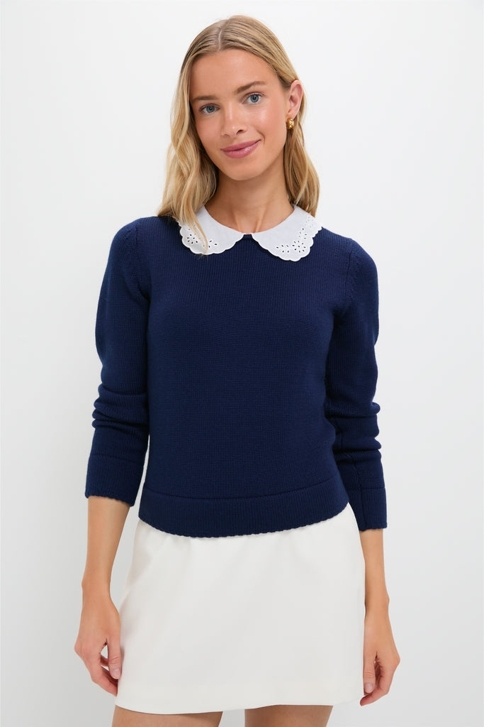 Young woman wearing the classic Navy Violette Sweater with eyelet collar and keyhole closure, styled effortlessly with a white skirt, embodying fun and high-end sophistication.
