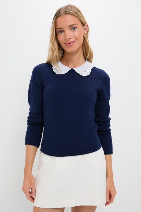 Young woman wearing the classic Navy Violette Sweater with eyelet collar and keyhole closure, styled effortlessly with a white skirt, embodying fun and high-end sophistication.